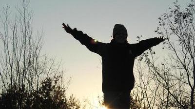 silhouette of a person with arms outstretched in front of the setting sun