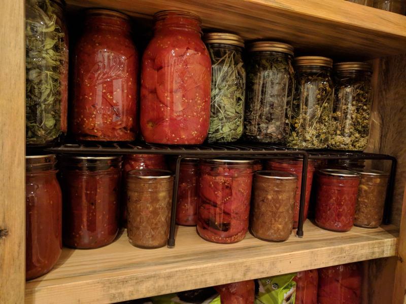jars of roasted tomatoes, jams, and herbs in a wooden cupboard