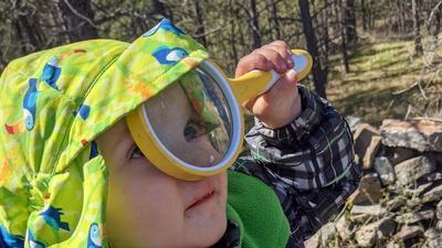 toddler holding a magnifying glass up to her eye and looking up at the sky