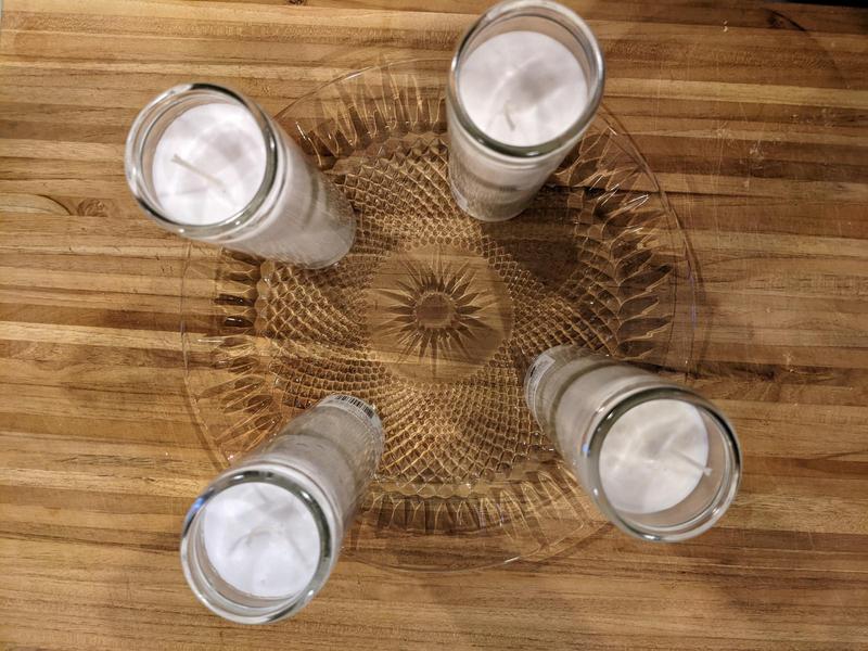top down view of four tall white candles on a glass plate