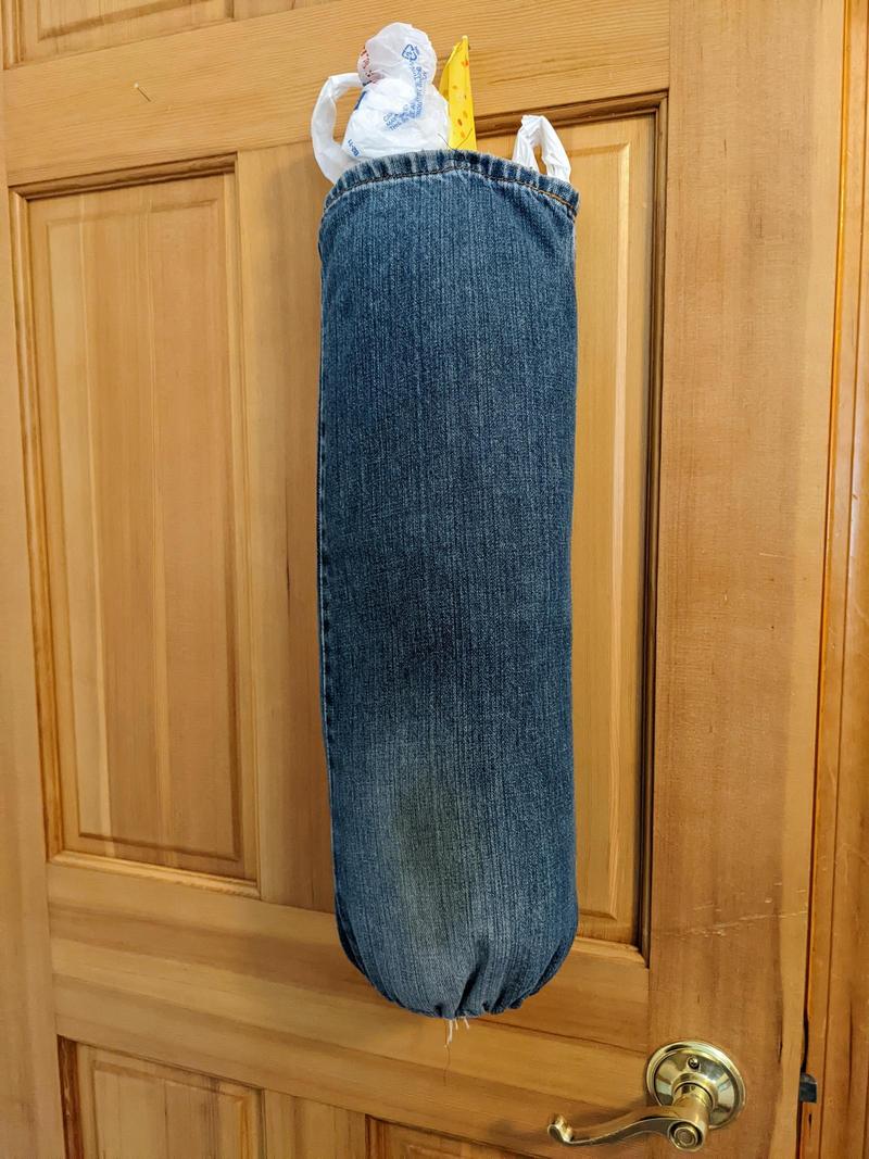blue jean fabric tube used as a plastic bag holder hanging on the back of a wooden door