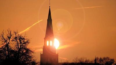 the sun rises behind the steeple of a church