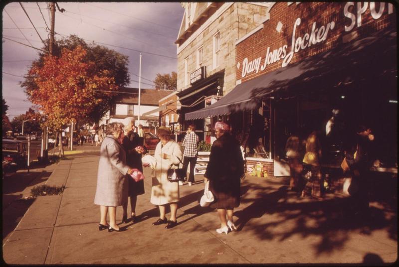 a few older women standing on a sidewalk outsie of some shops in the downtown of a small town