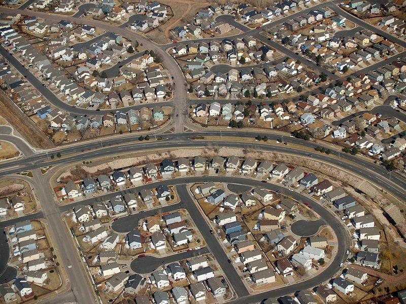 aerial view of classic suburbs with rows of boxy houses along curving roads and culdesacs, with no greenery to be seen