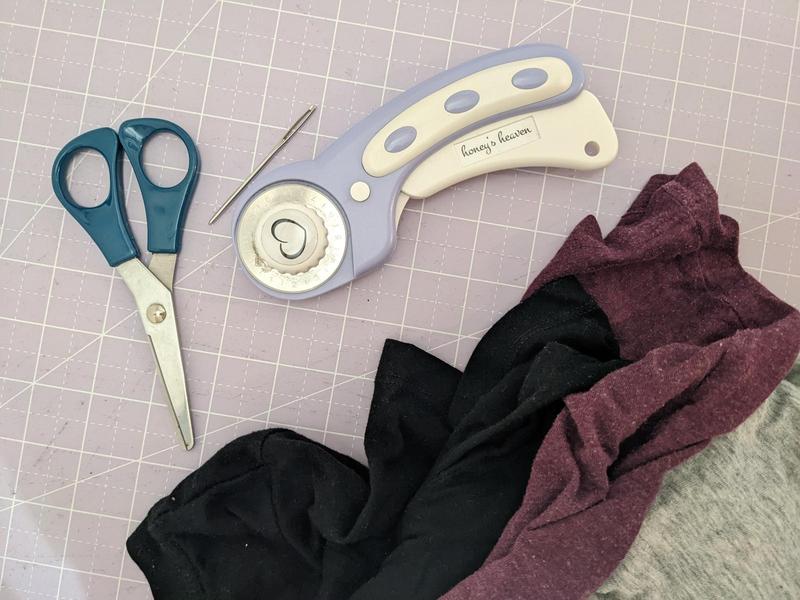 scissors, a rotary cutter, a tapestry needle, and some tshirts on a cutting mat