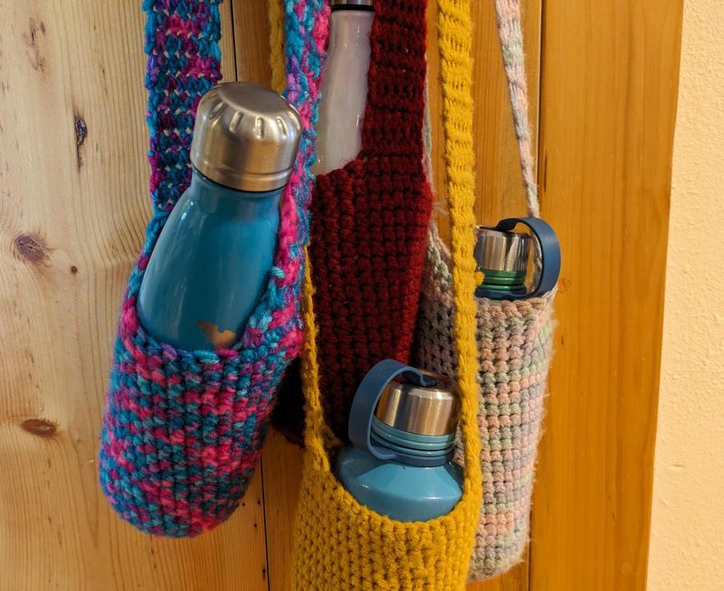 four crochetted water bottle carriers with water bottles in them