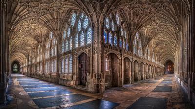 the cloisters at gloucester cathedral: the intersection of two long stone hallways lined with windows, stained glass, and elaborate archways